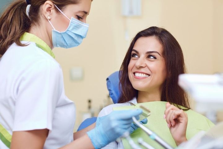 Woman in a dental chair smiling at a dentist wearing a mask and gloves in a dentist's office.