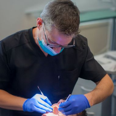 Person in medical scrubs and mask using a computer, wearing surgical loupes.