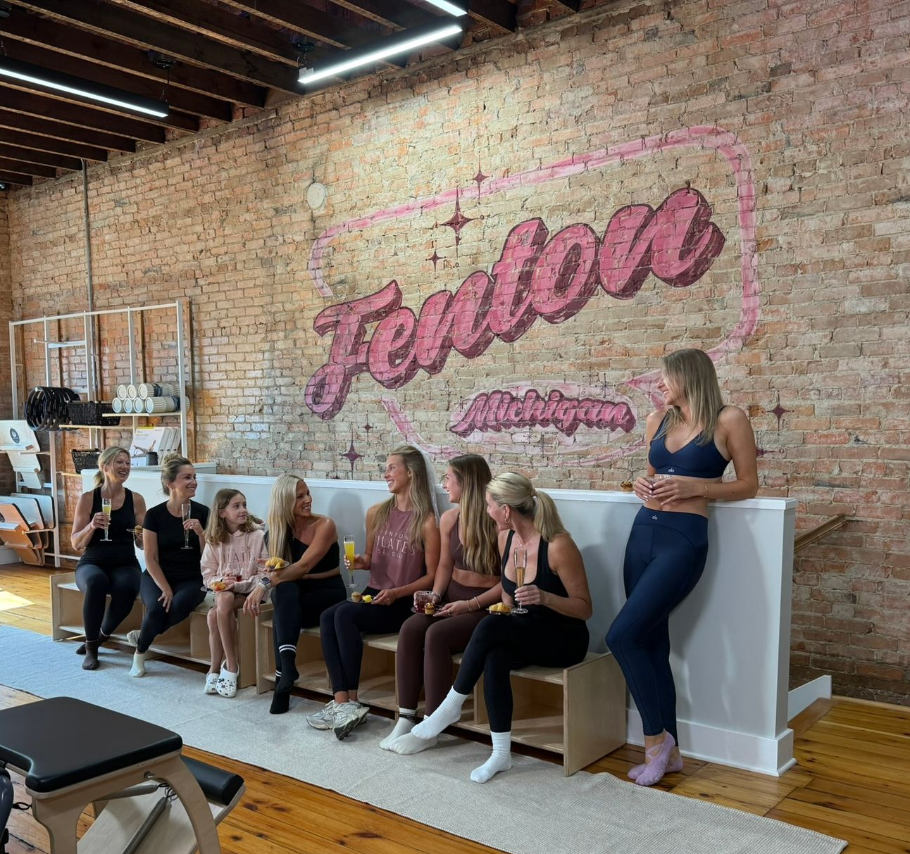Pilates class stretching on reformer machines in a brick-walled studio with arched windows