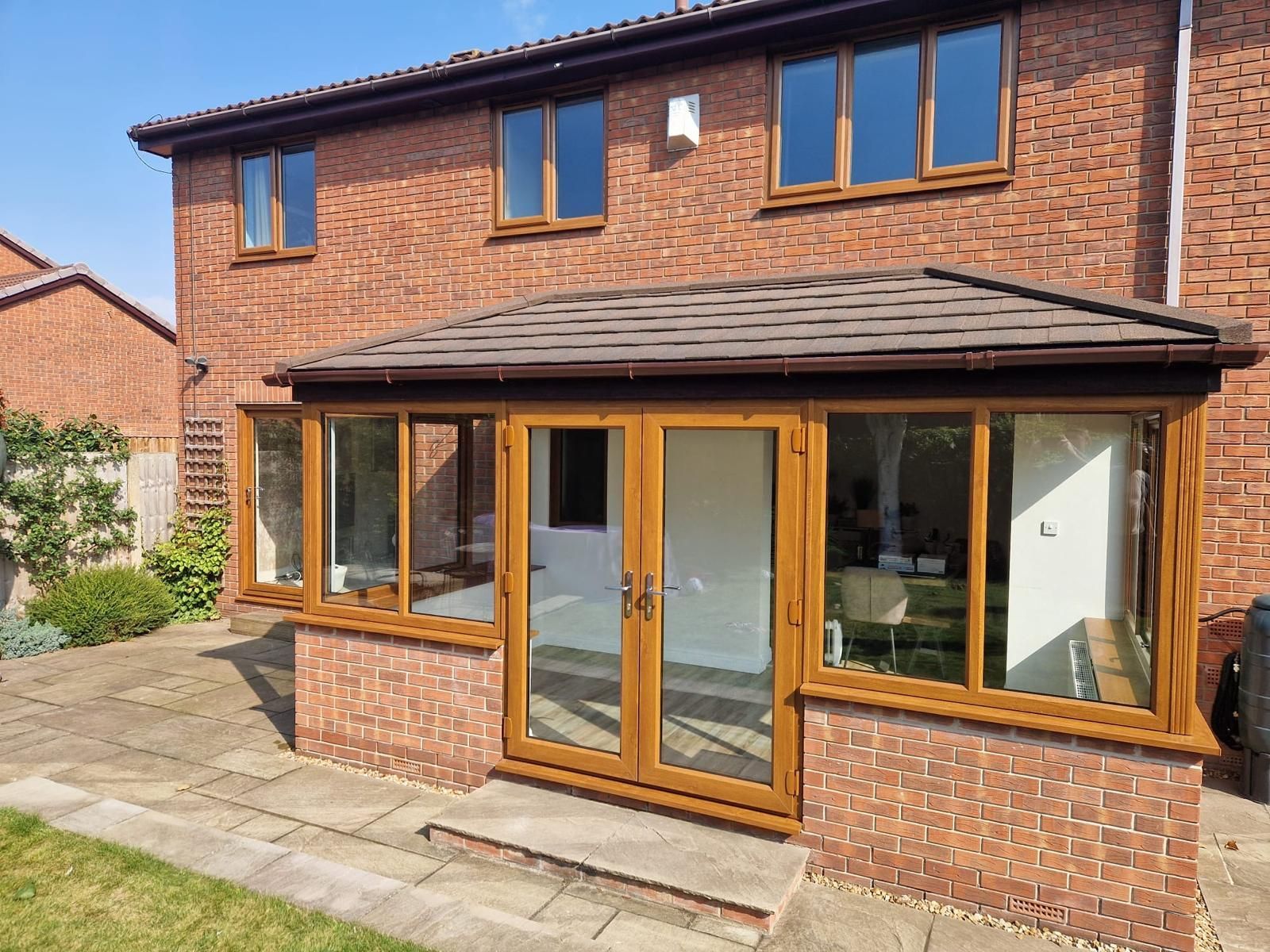 Brick two-story house with a wood-framed glass sunroom and patio doors in front.