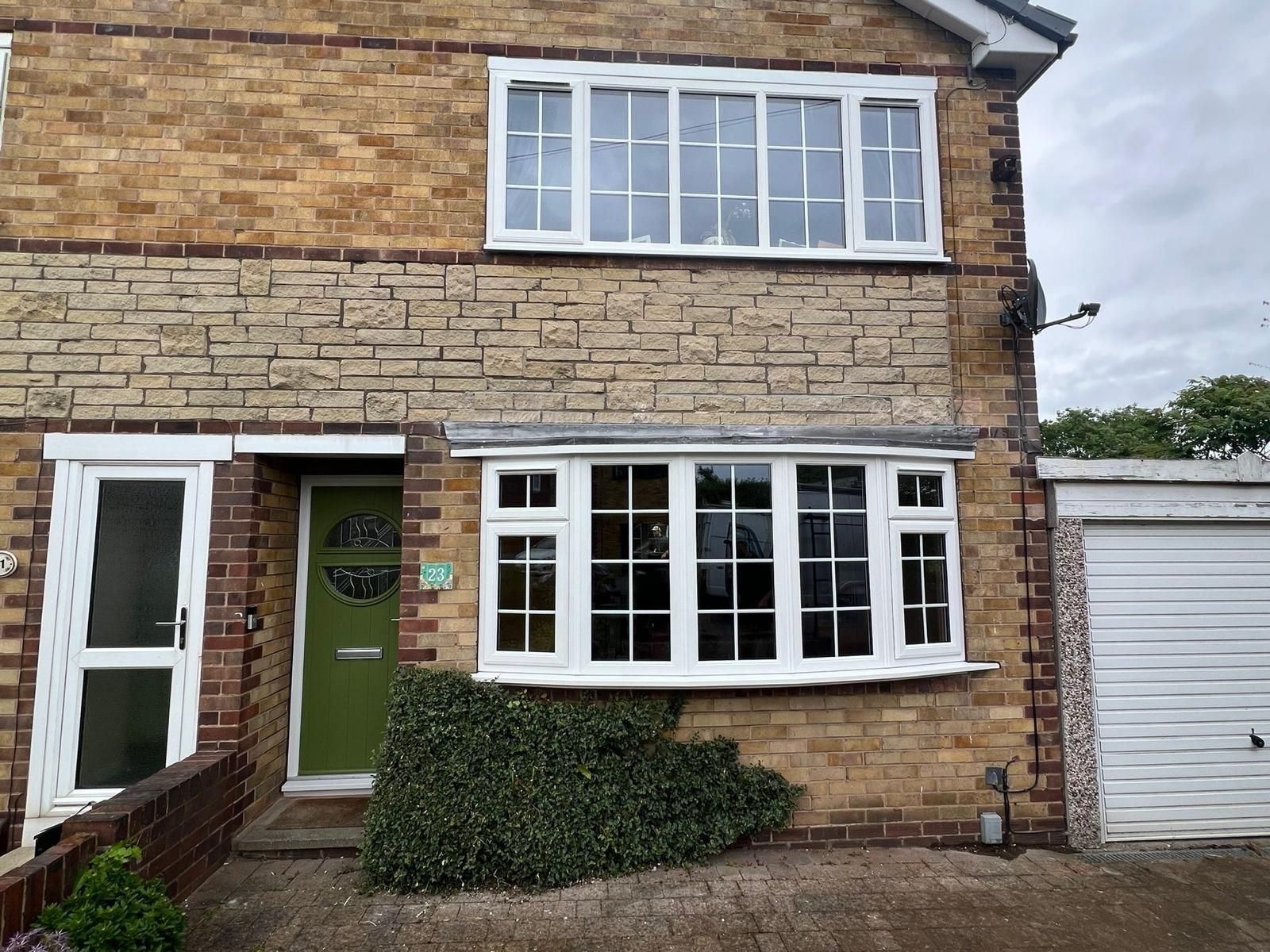 Stone-and-brick house exterior with green front door, white bay window, upper windows, and garage door