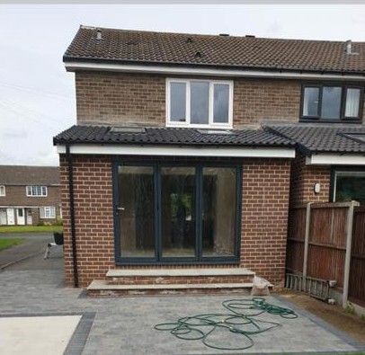 Front view of a brick house with a glass porch, driveway, and coiled green hose on the ground