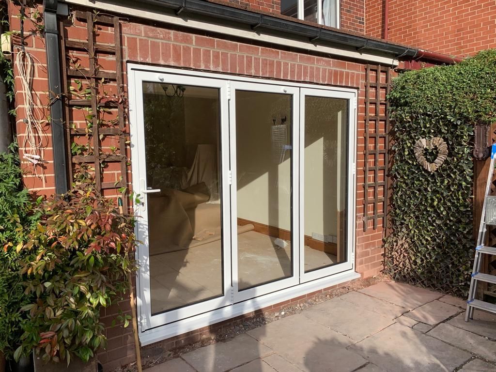 White sliding glass doors on a red brick patio with sunlit hedges and potted plants