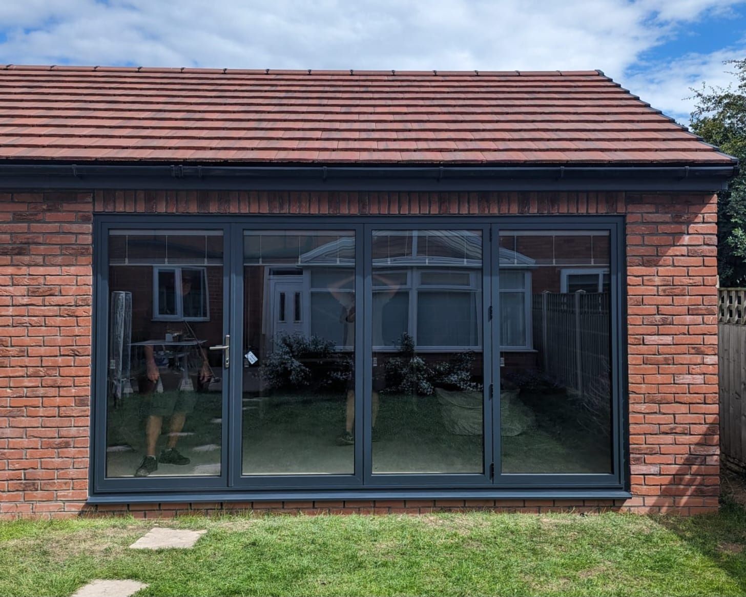 Modern brick house exterior with large black-framed glass patio doors under a red-tiled roof