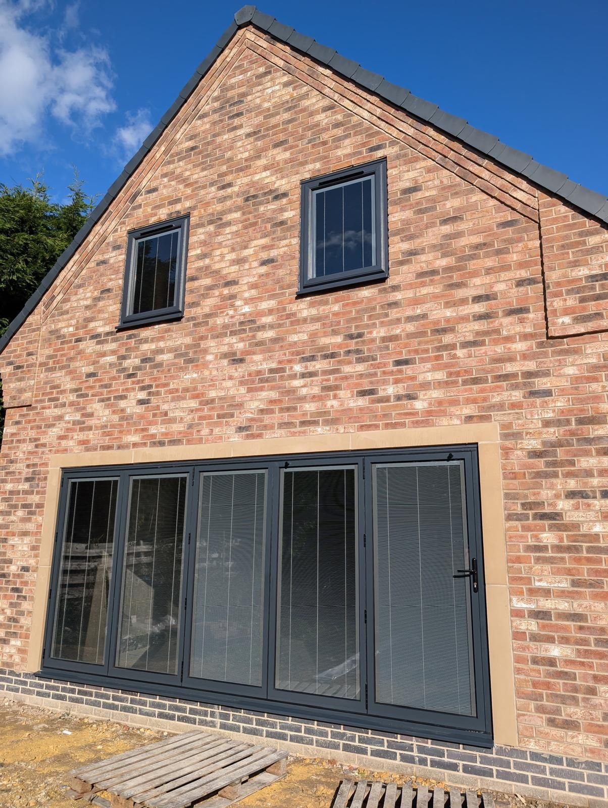 Brick house exterior with black-framed patio doors and two upper windows under a gabled roof.