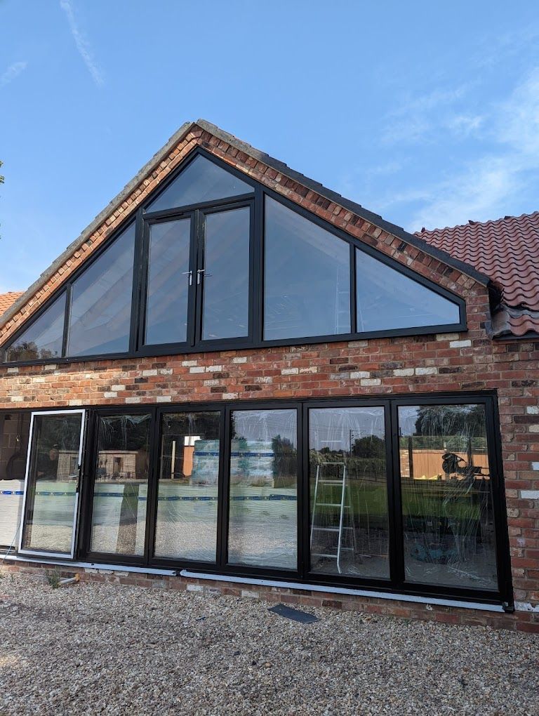 Brick house with large black-framed glass windows and a steep gable roof under a blue sky
