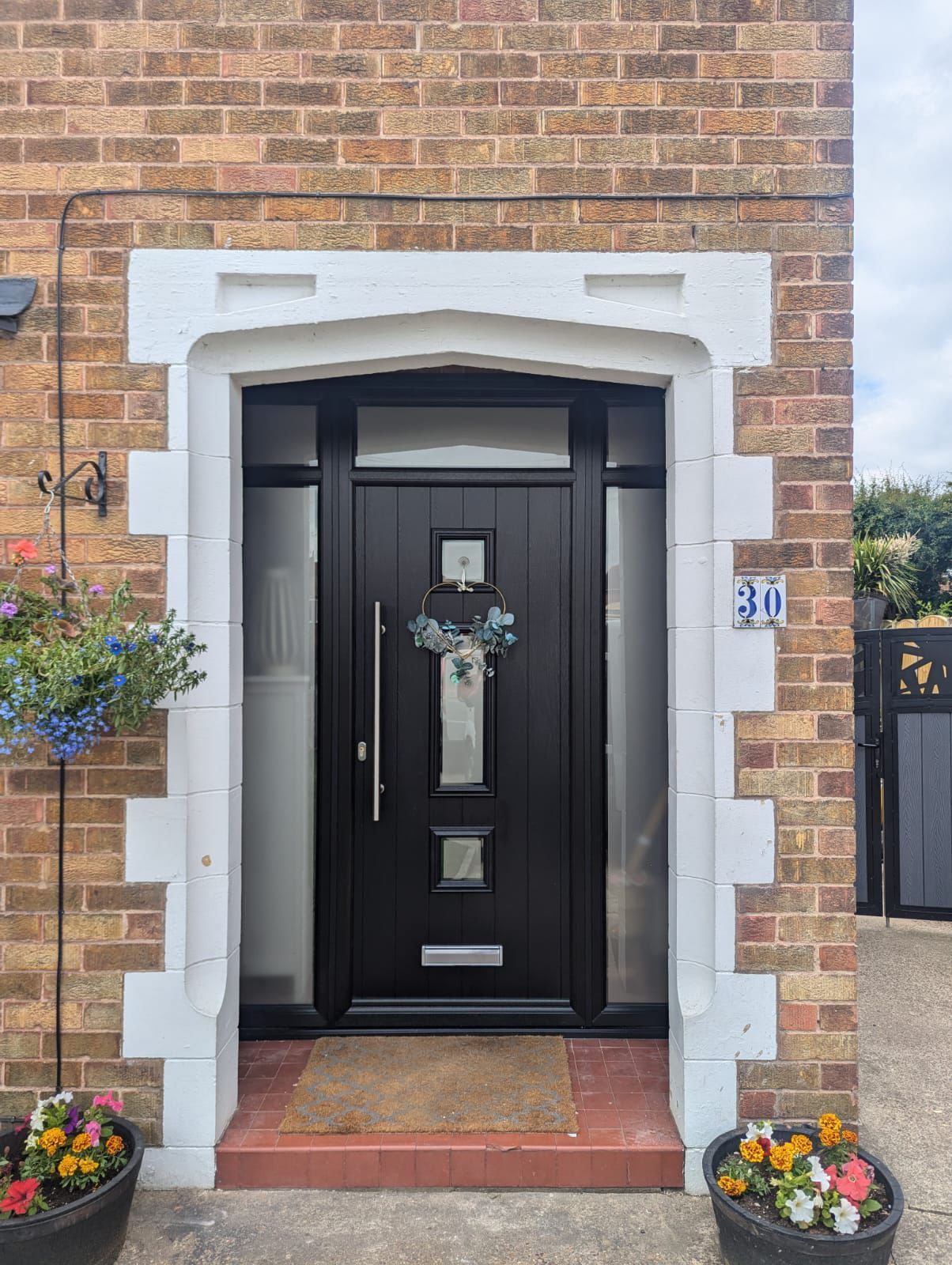 Front door of a brick house with white trim, black door, and flower pots by the steps.
