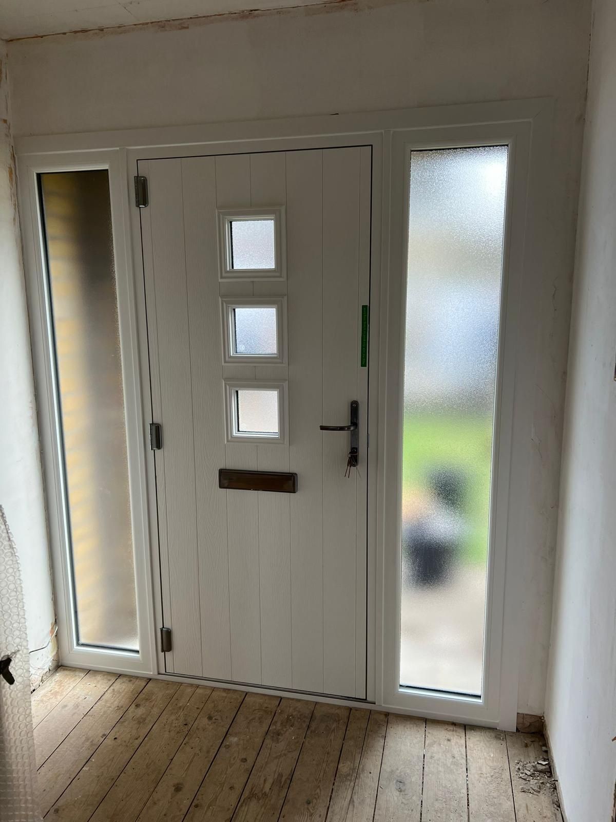 White front door with frosted glass sidelights and three square windows in a narrow entryway
