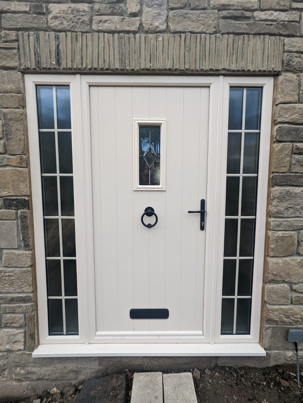 White front door with narrow sidelights set in a stone exterior wall