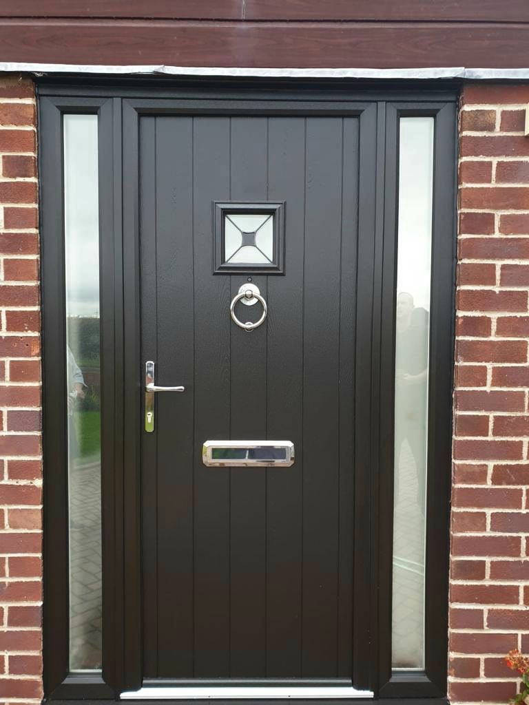 Black front door with narrow frosted side panels and brass mail slot in a brick wall