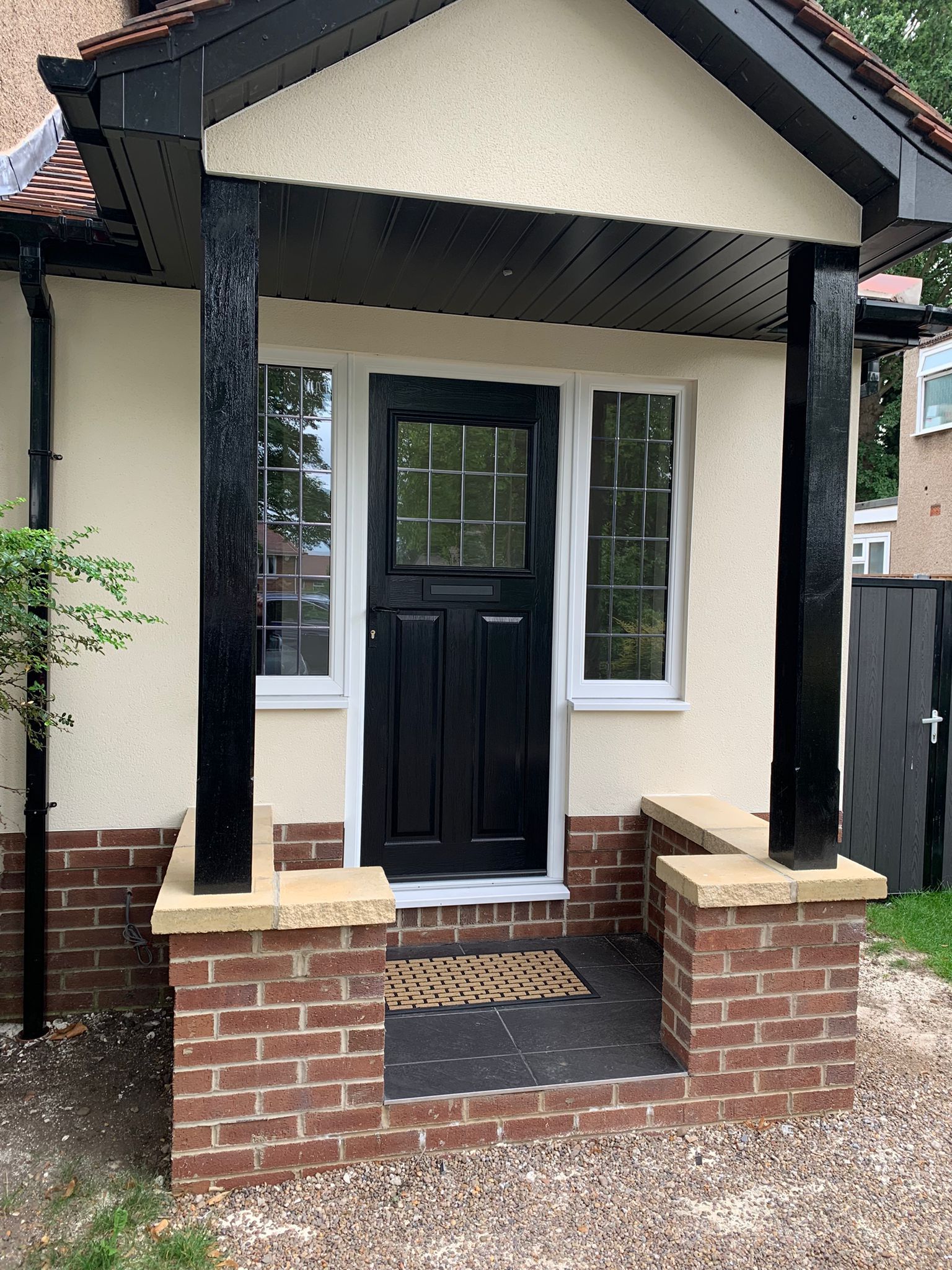Front porch with black front door, white trim, brick steps, and a small covered entryway.