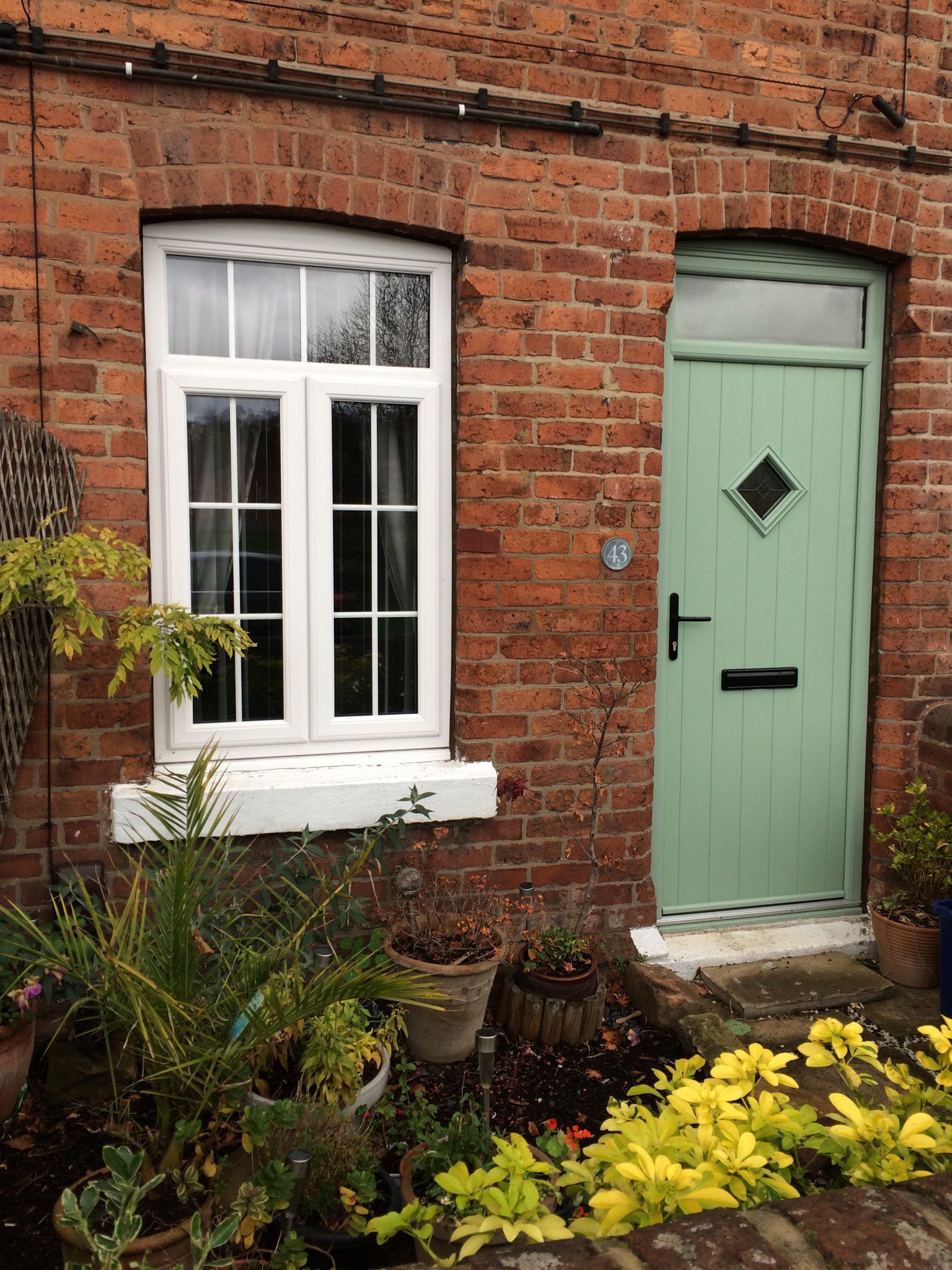 Brick house facade with white window, mint-green door, and colorful flower beds