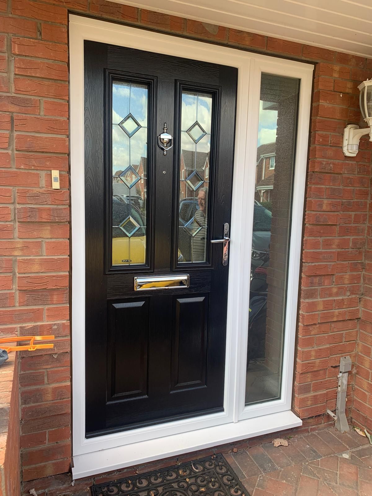 Black front door with frosted glass panels and white side window in a brick exterior wall