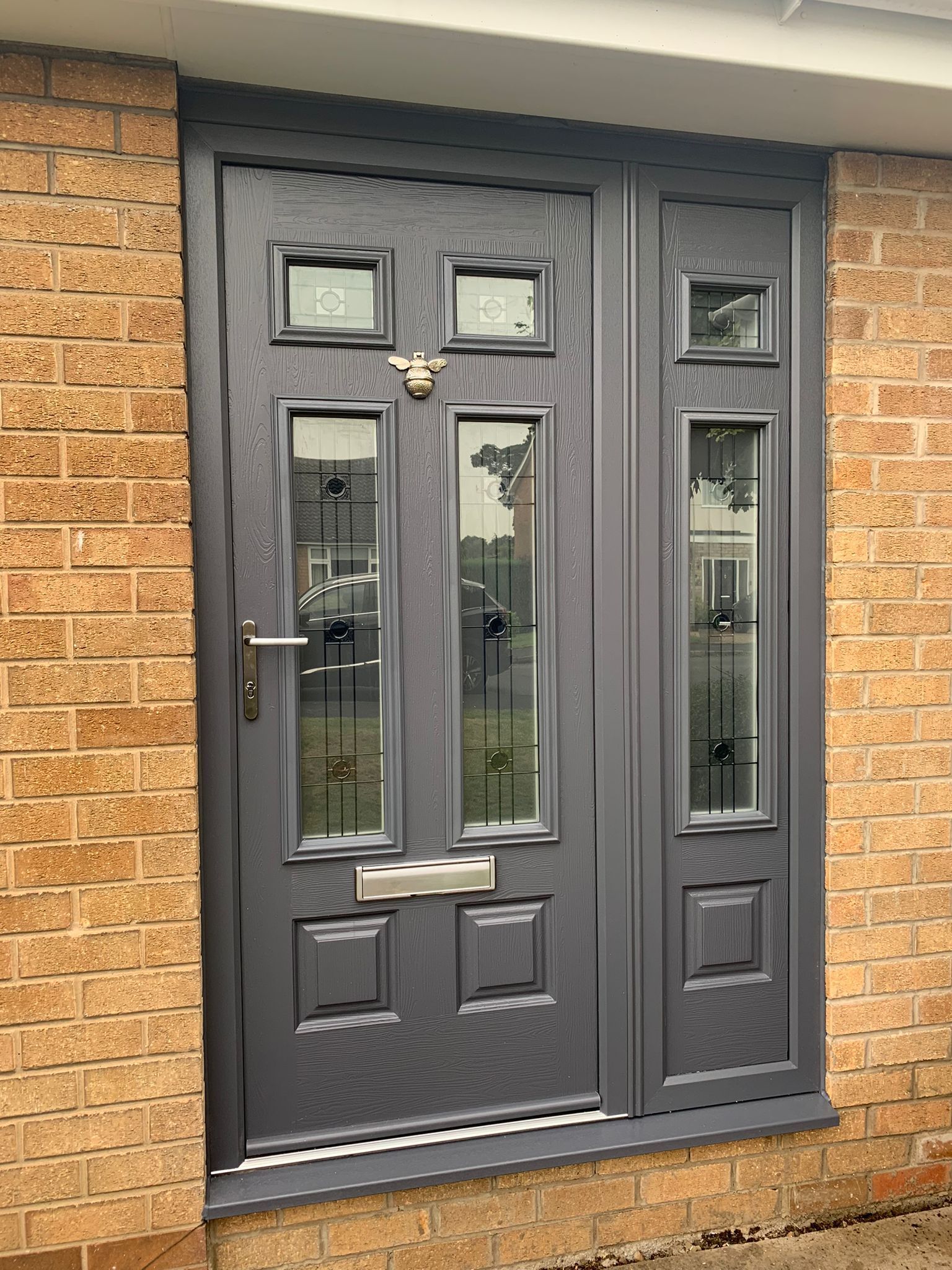 Dark gray front door with sidelights and brass knocker set in a brick entrance.
