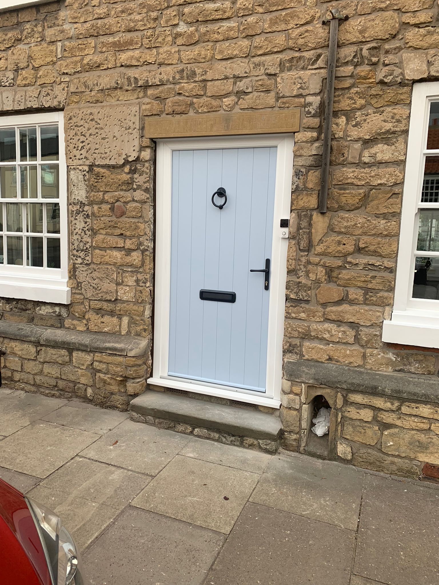 White front door with black handle set in a stone building, flanked by windows on a sidewalk.