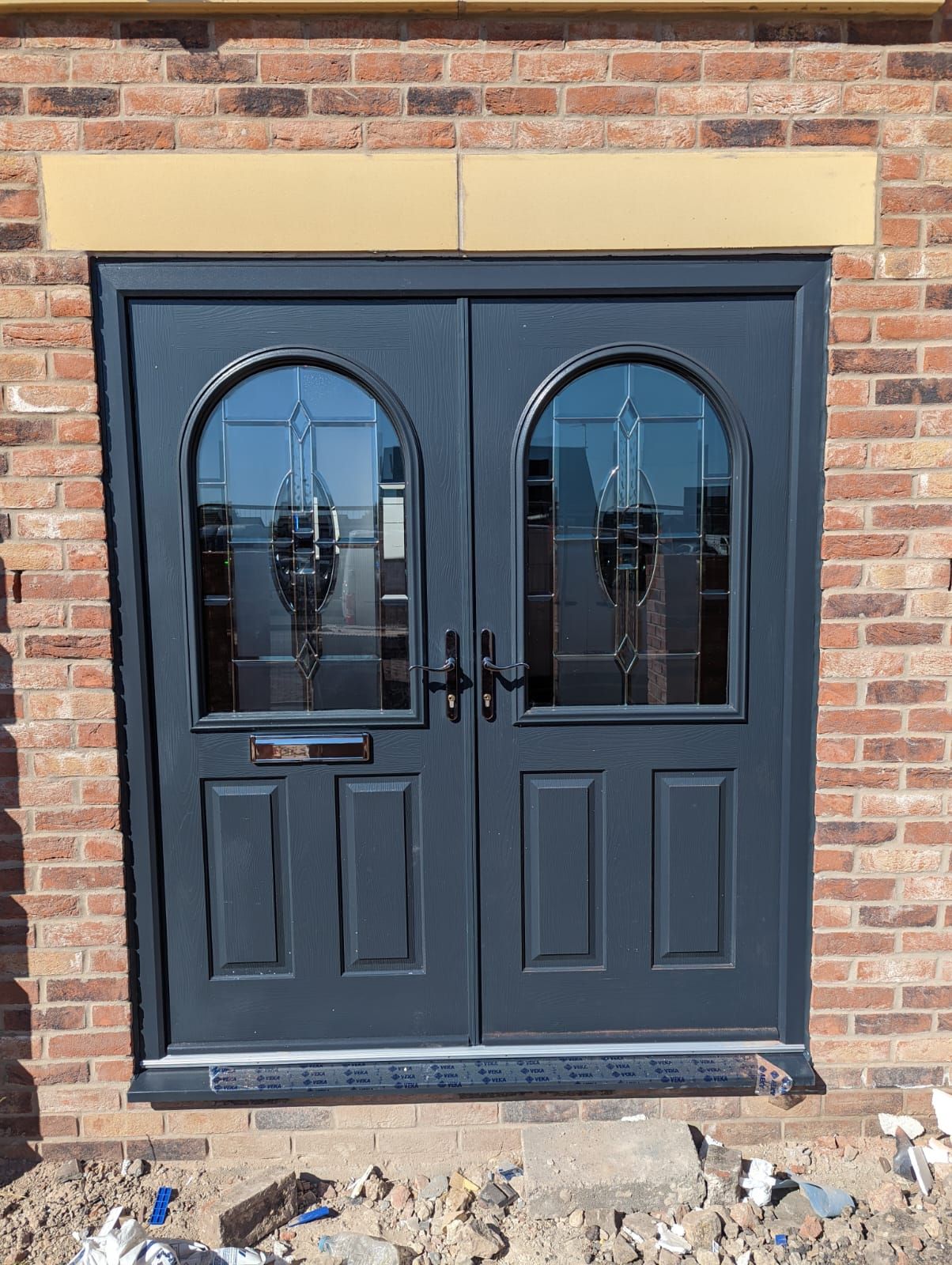 Dark double front door with arched windows set in a brick wall, with construction debris below.