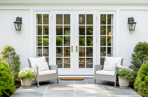 Front patio with white French doors, two gray chairs, potted plants, and wall lanterns