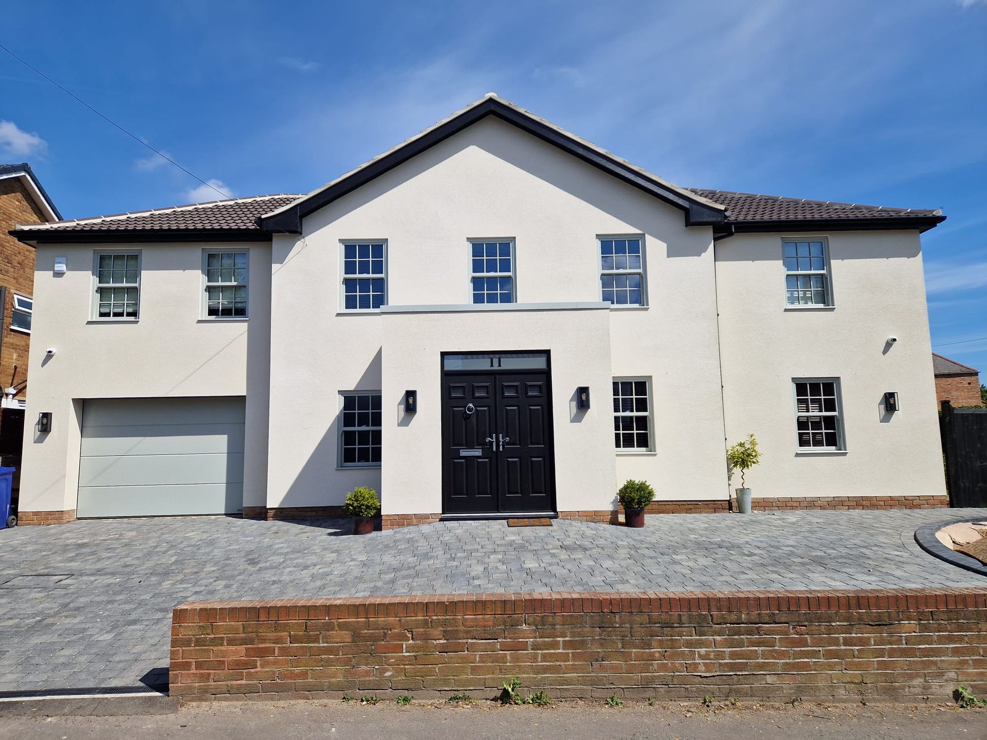 Two-story cream house with black front door, garage, and paved driveway under a blue sky