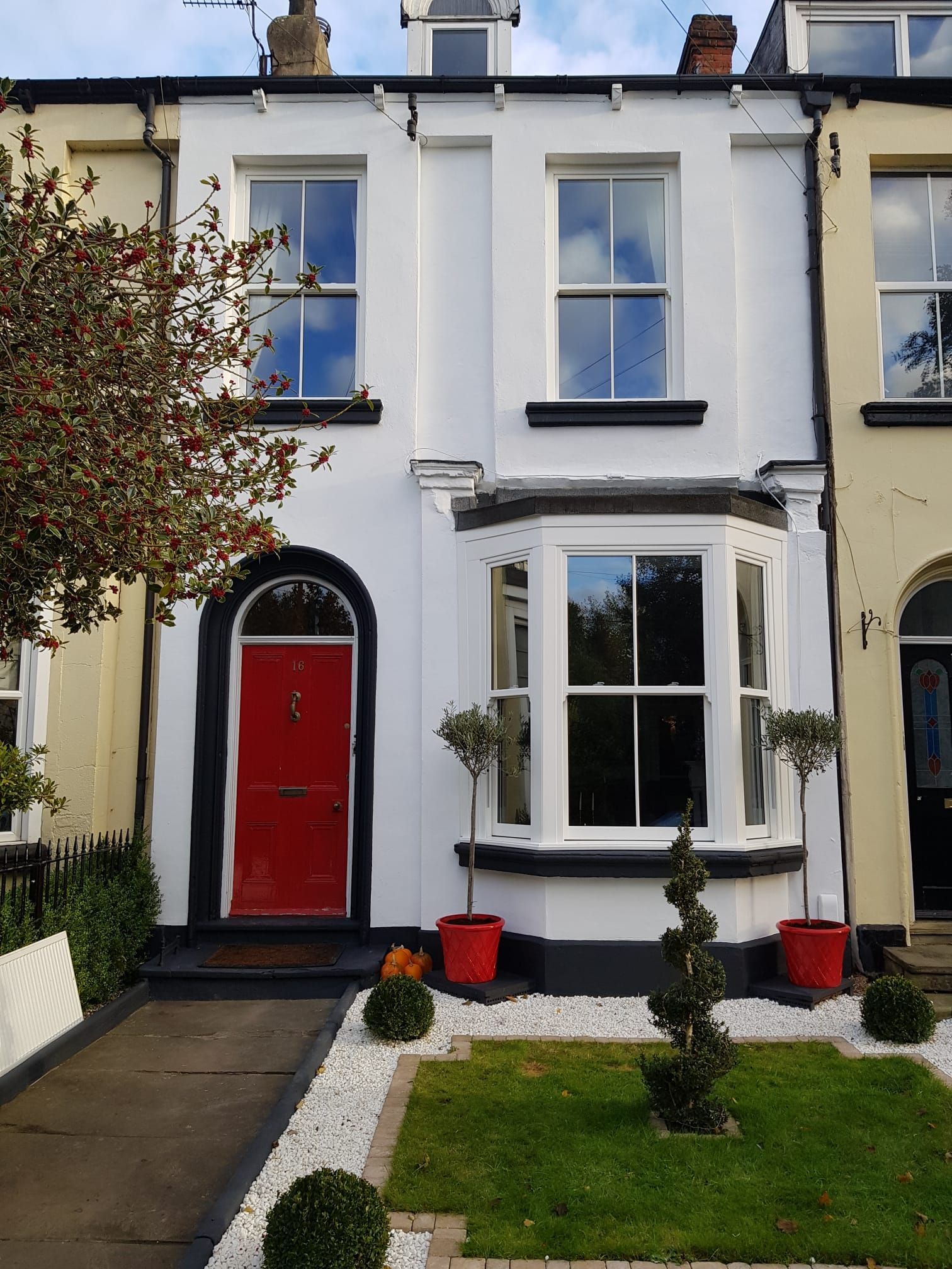 Two-story white townhouse with a red front door, bay window, and small front garden.