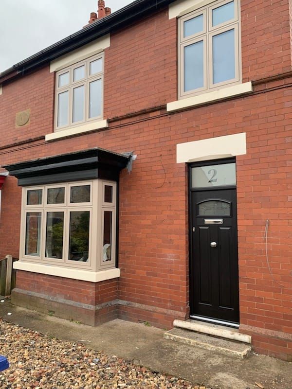 A red brick house exterior with a black front door, a black bay window roof, and beige-framed windows.