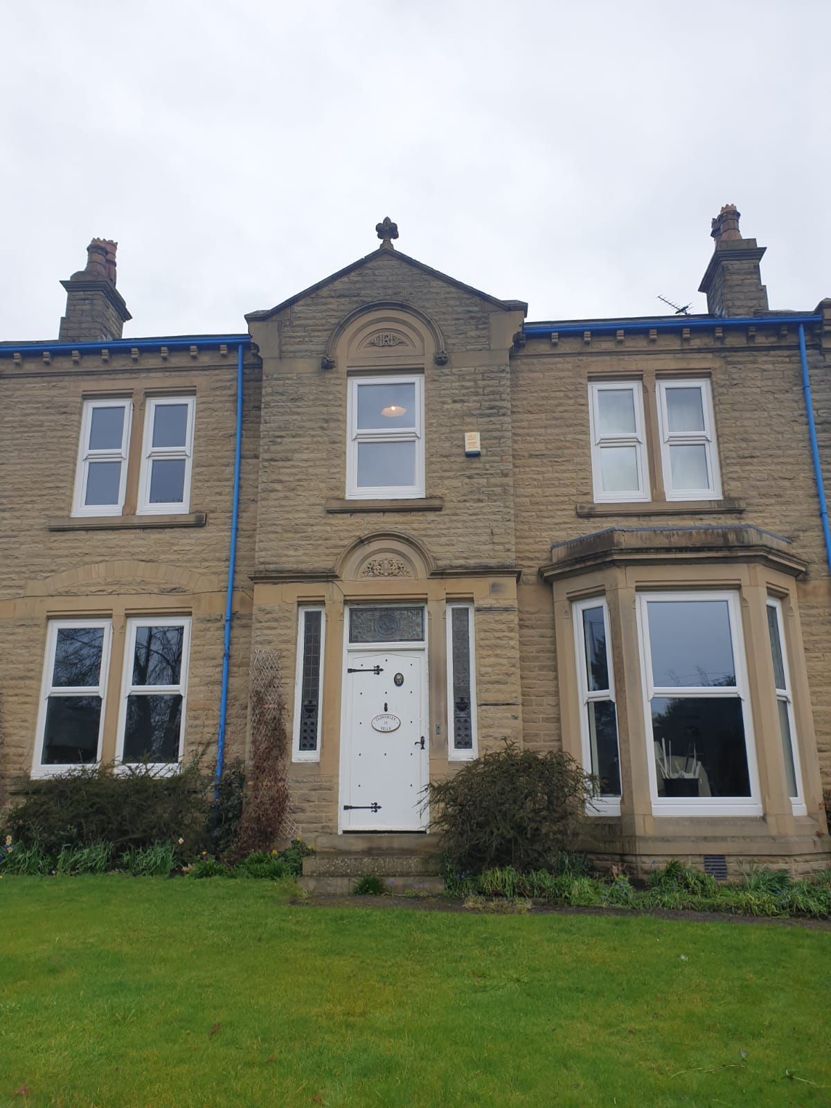 Stone townhouse facade with white door, bay windows, and green lawn under an overcast sky