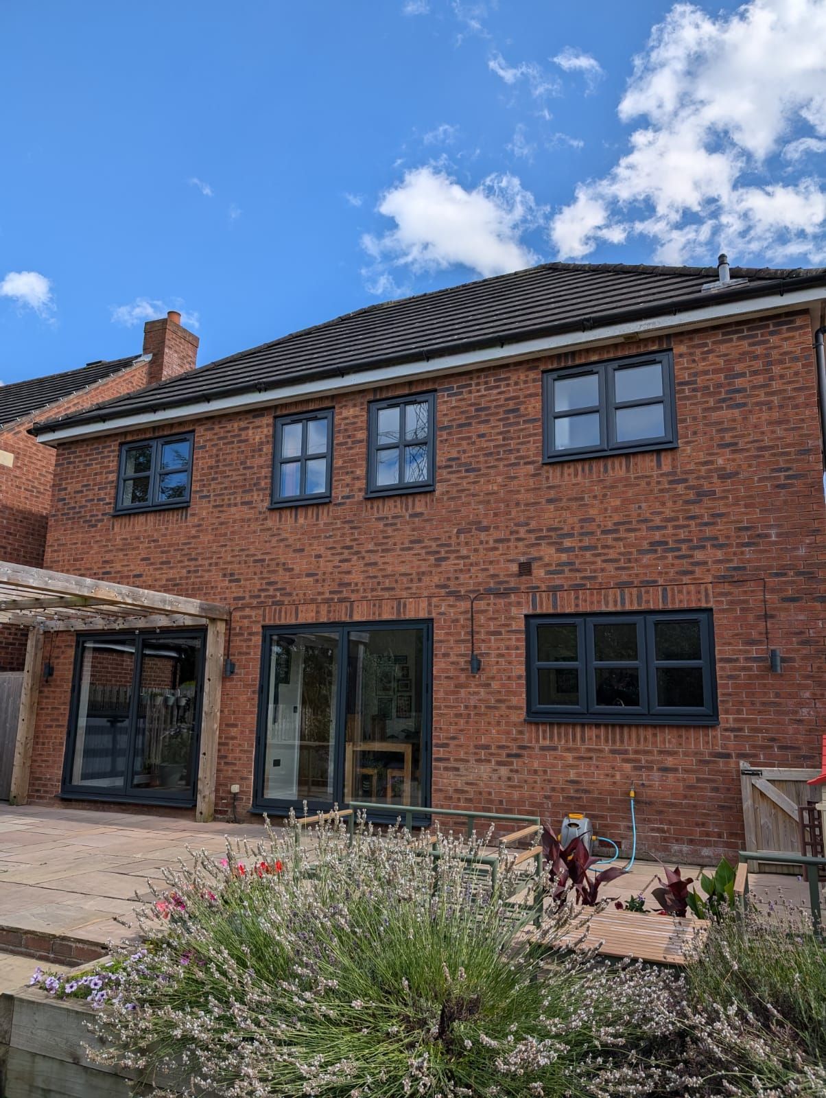 Brick house with dark-framed windows, patio doors, and a garden under a blue sky