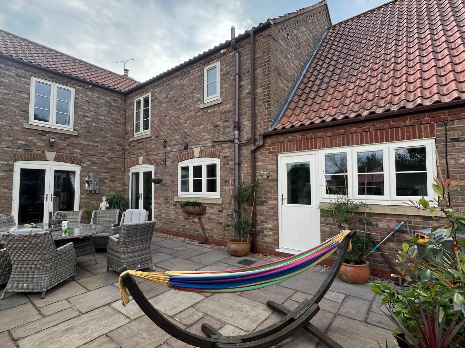 Brick courtyard patio with white doors, wicker chairs, and a rainbow hammock chair