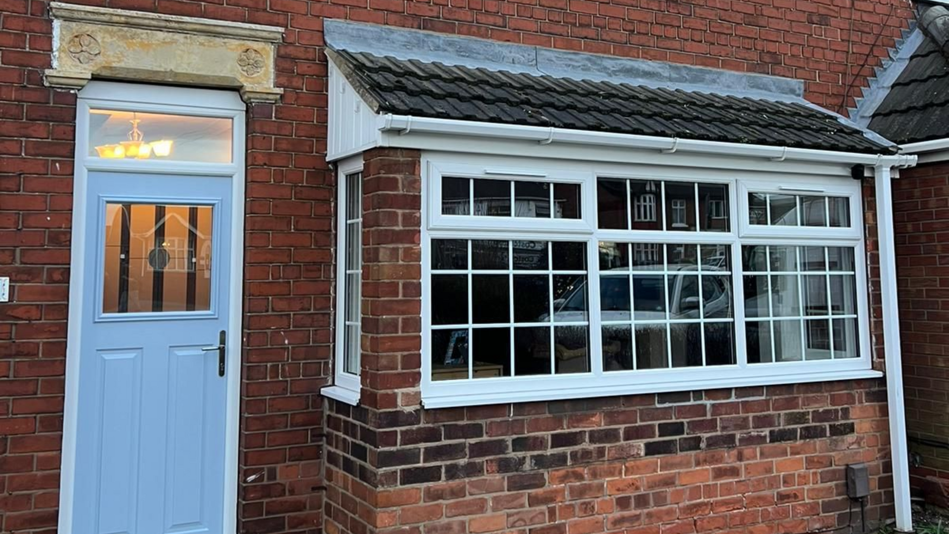 Light blue front door beside a red brick house with a white-trimmed bay window.