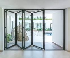 Folding glass doors open to a patio with white furniture, plants, and a pool.