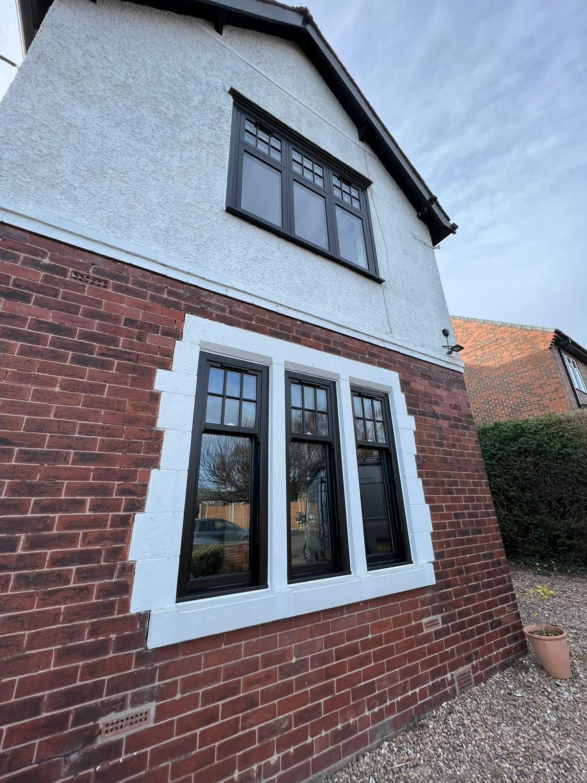 Two-story brick house exterior with white render and black-framed windows