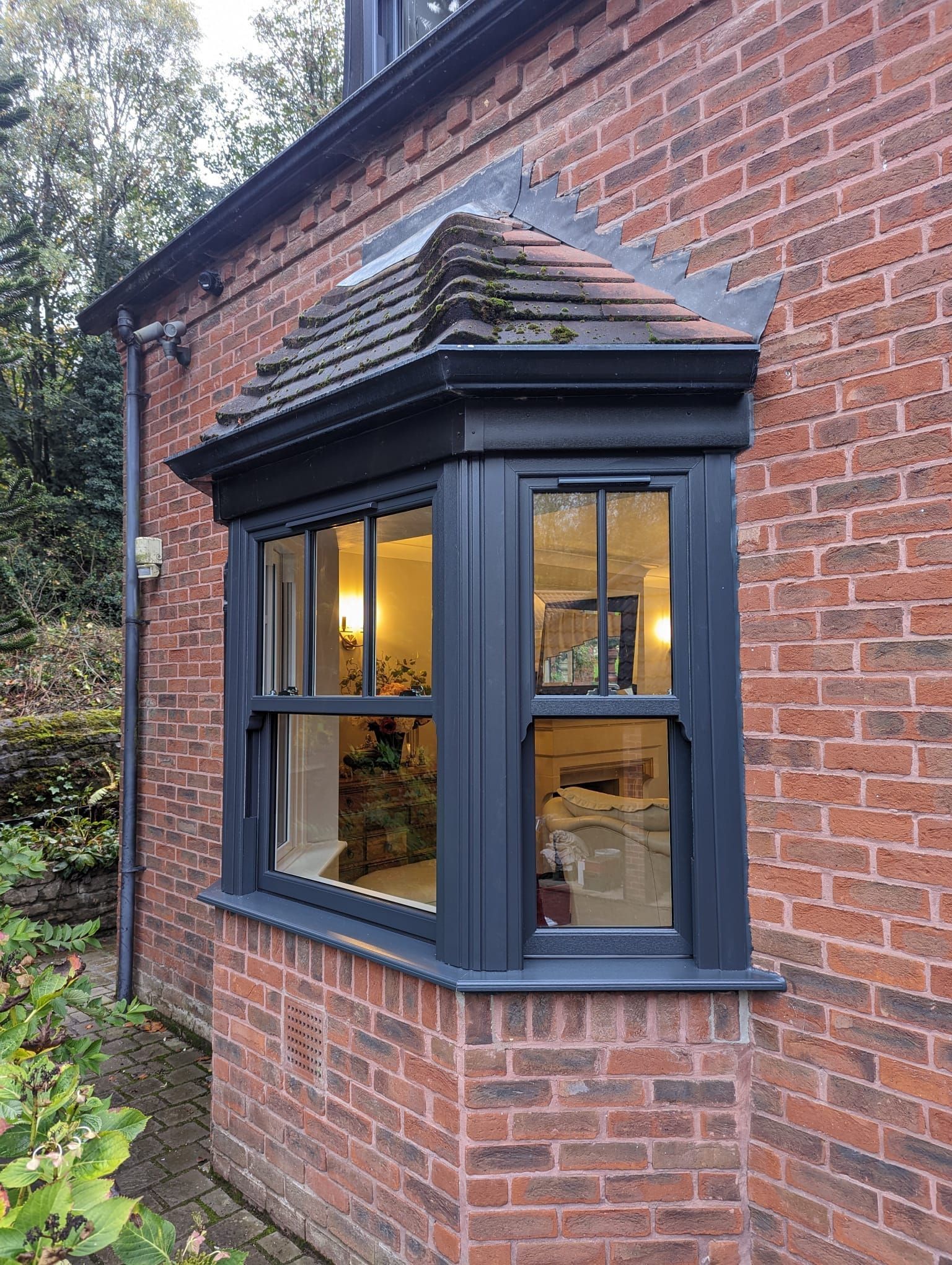 Brick house bay window with black trim and warm lights glowing inside