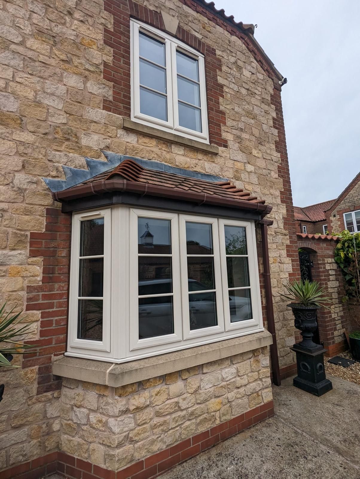 Stone house exterior with white bay window and tiled roof under a cloudy sky