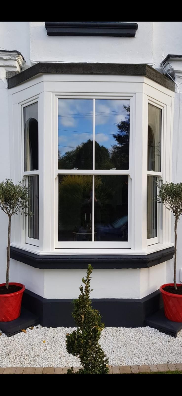 White bay window with black trim and red planters on a house exterior
