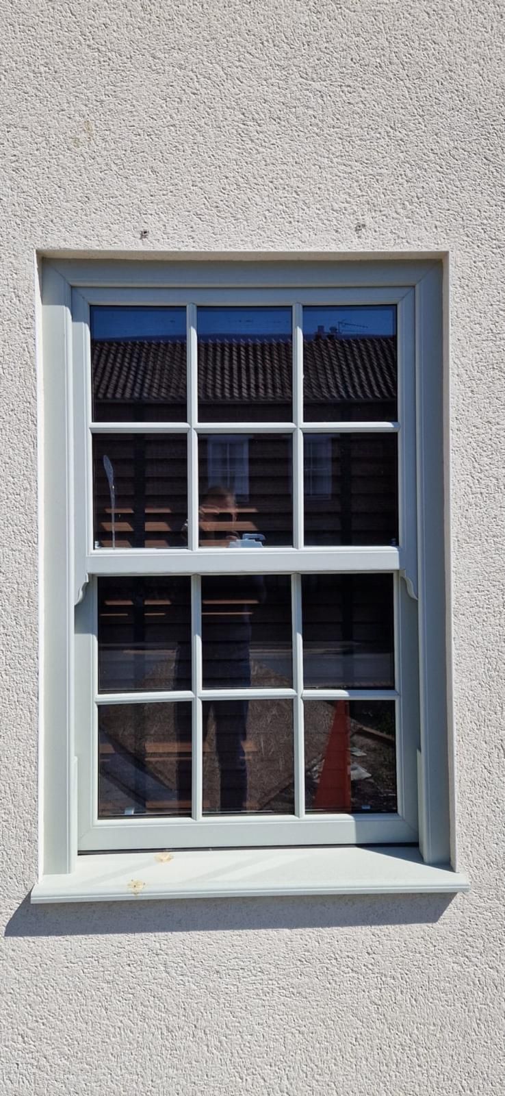 White-framed window with blue trim on a textured light wall, reflecting the sky and nearby buildings