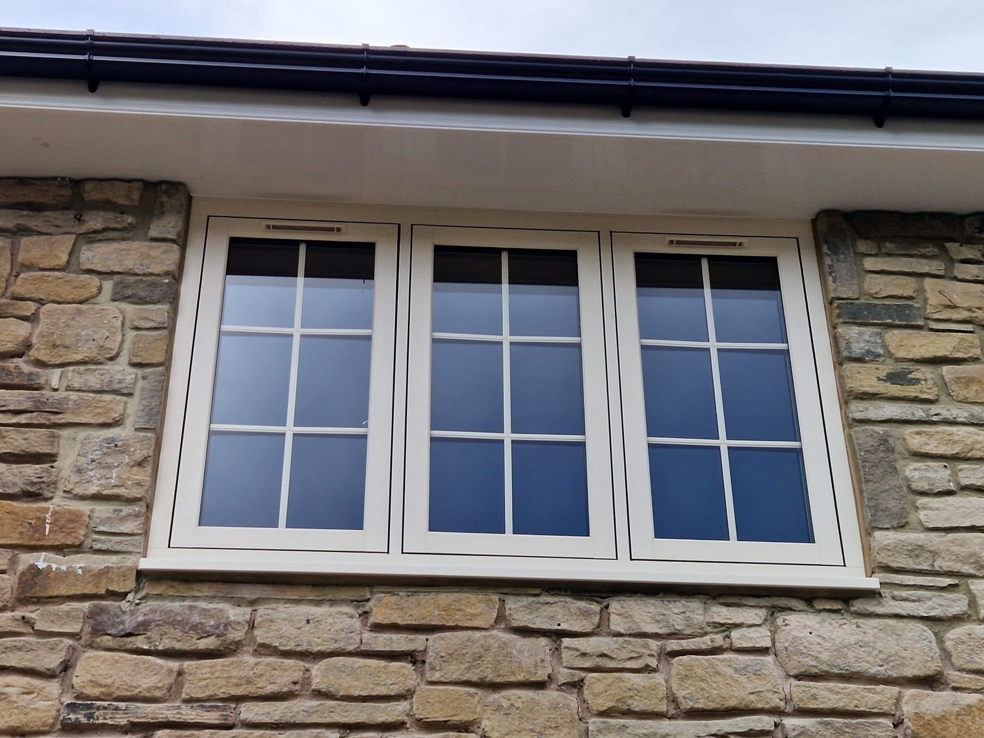 White-framed window set in a stone wall beneath a dark roof eave