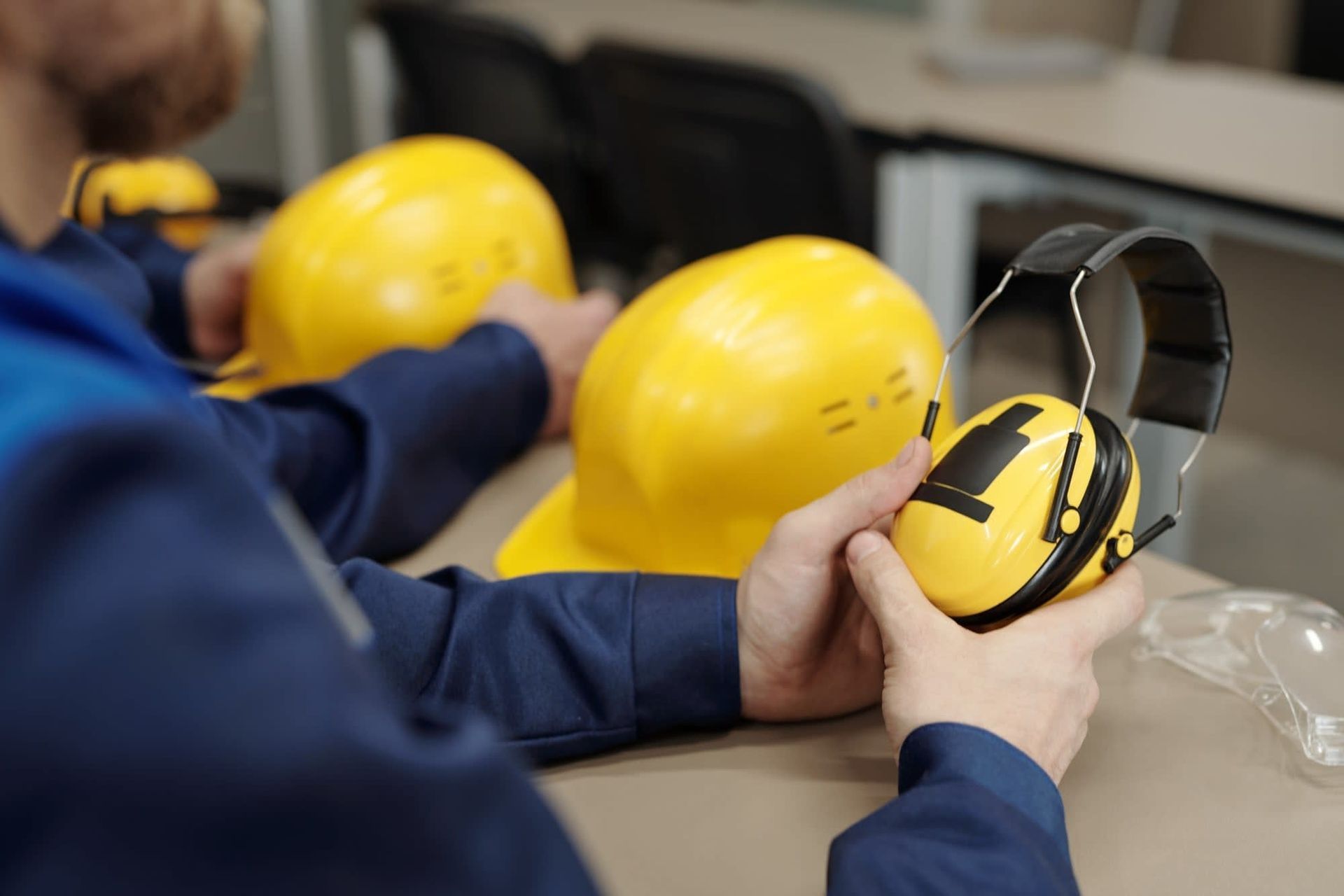 Worker fitting yellow hard hat ear muffs at a workbench
