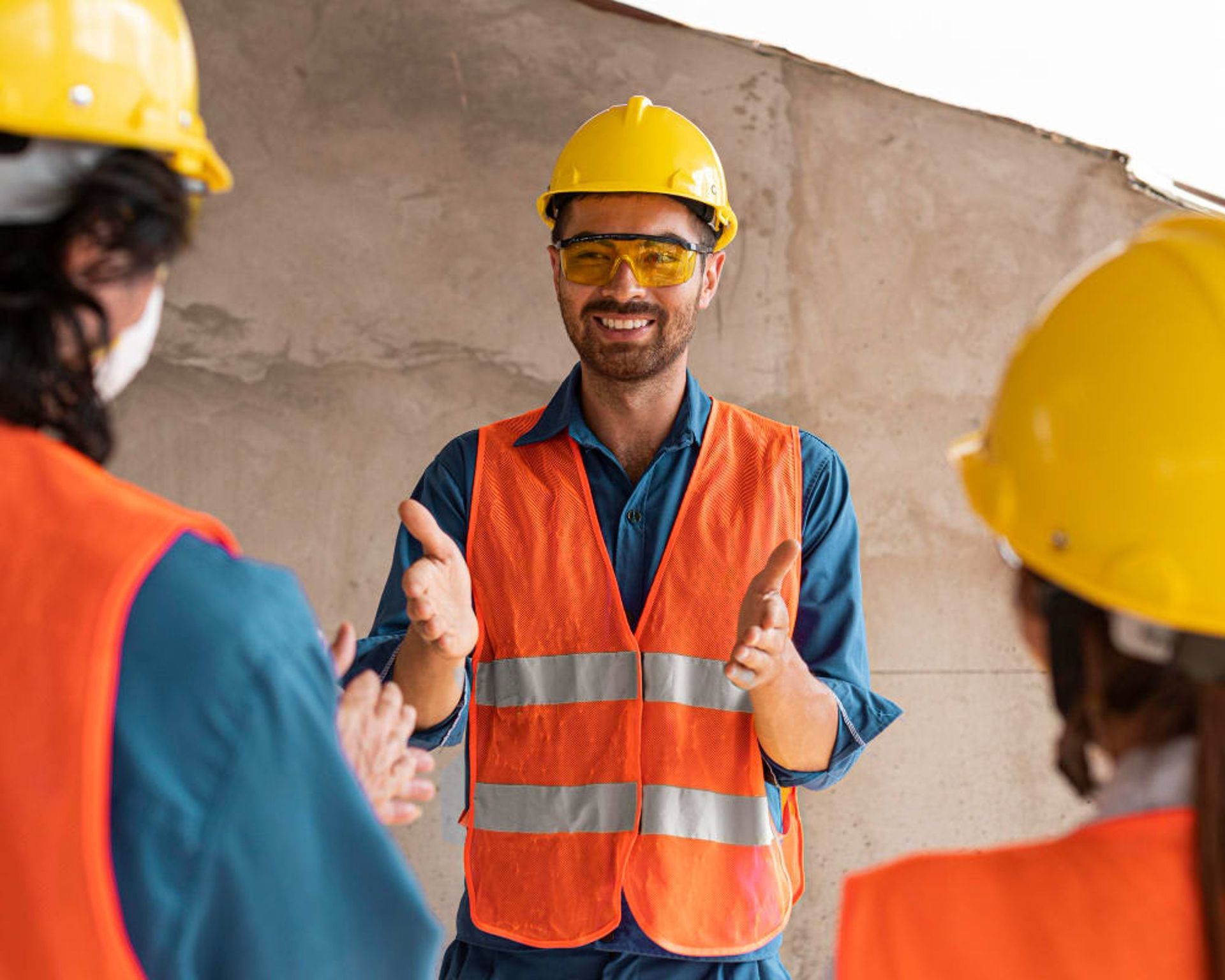 Construction worker in yellow hard hat and orange vest giving a thumbs-up on a job site