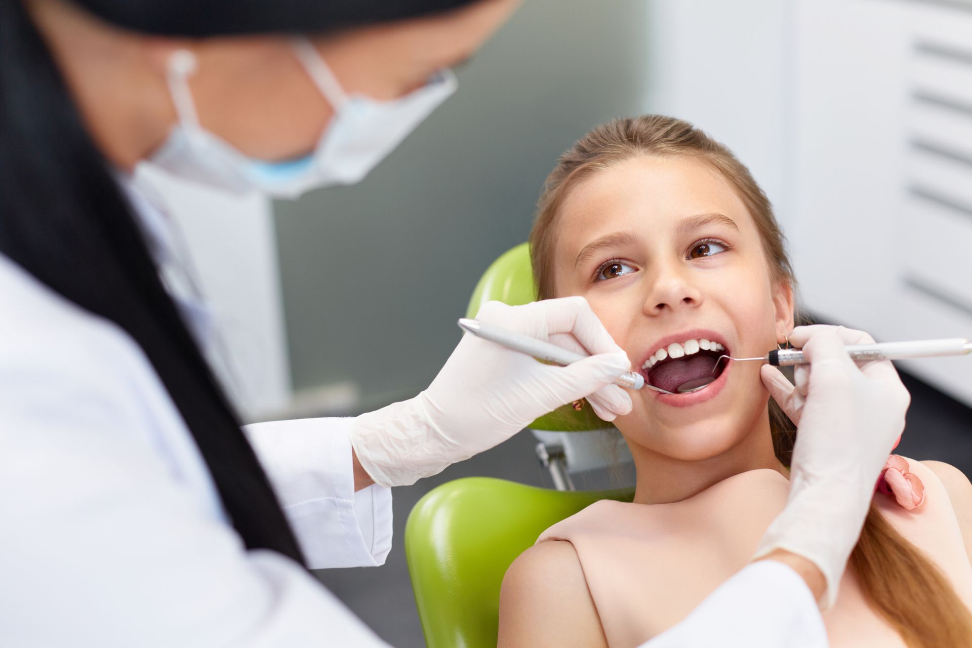 Una ragazzina è seduta sulla poltrona del dentista mentre un dentista le visita i denti.