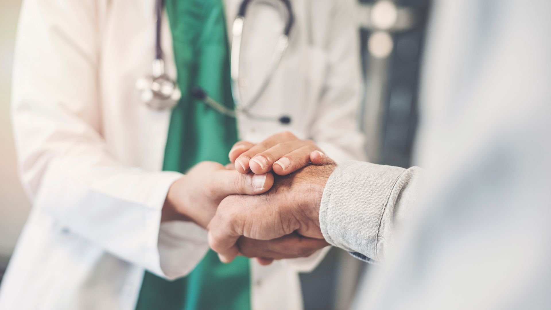 Doctor holding patient's hand for comfort, stethoscope visible.