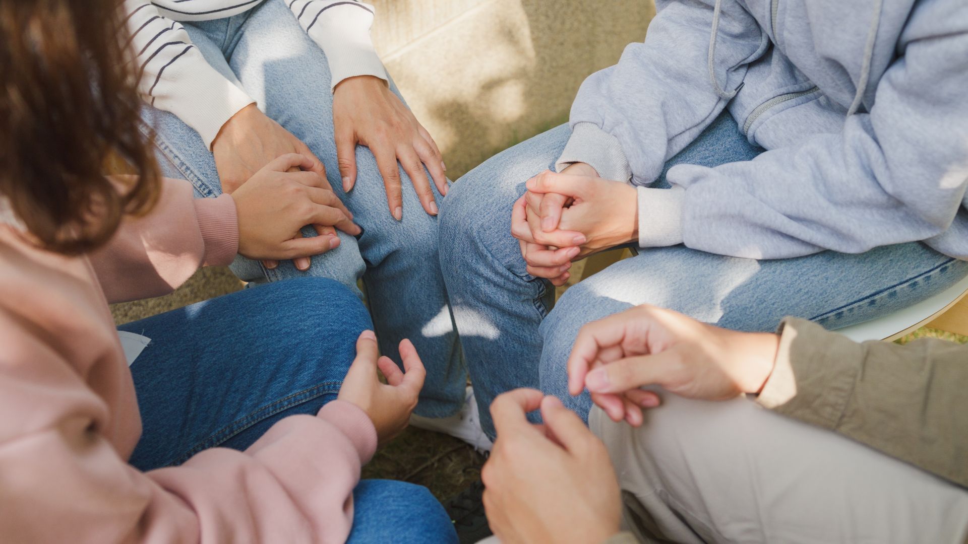People seated in a circle, holding hands, likely in a supportive group.