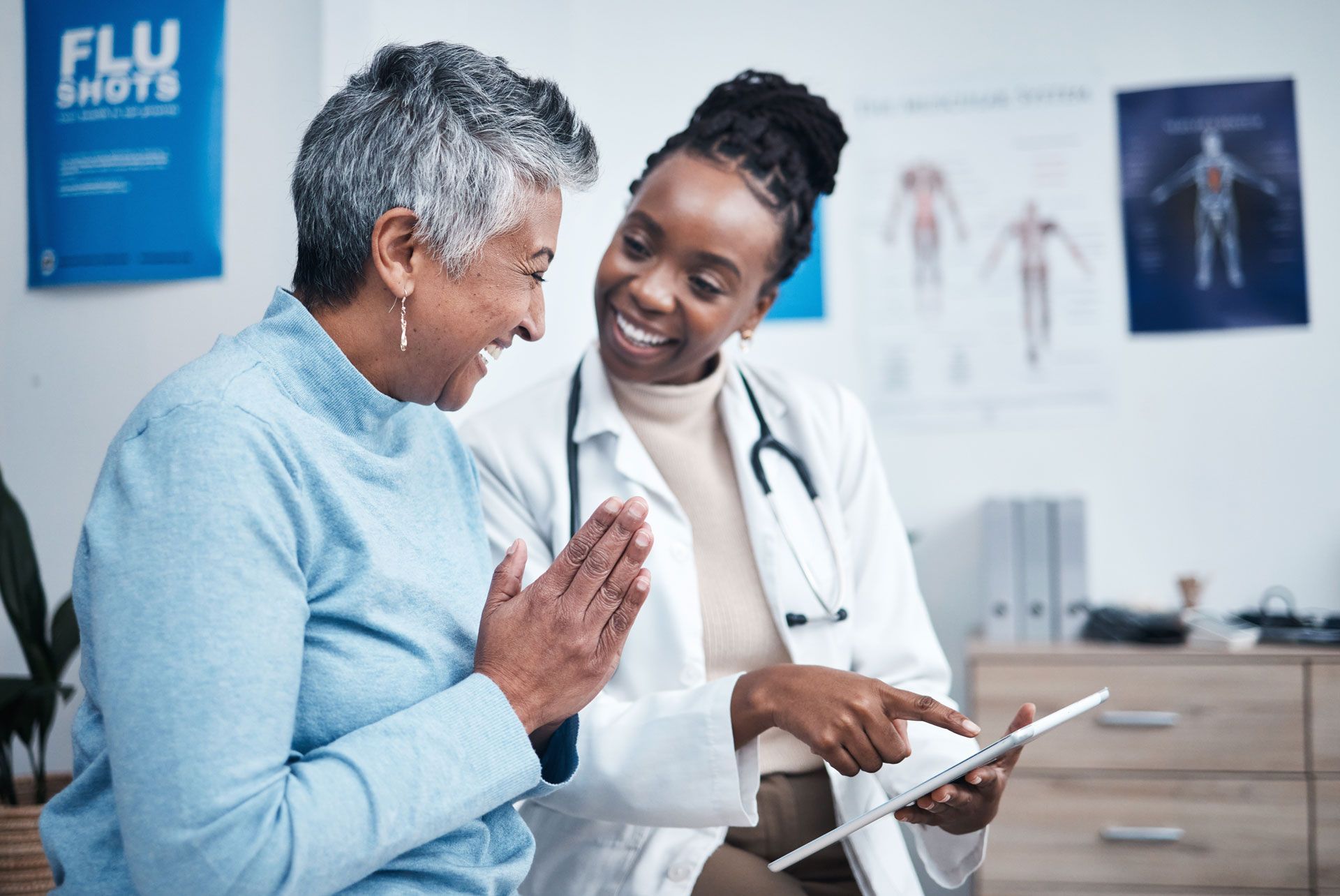 A doctor in a white coat showing a tablet to a smiling patient in a bright medical office.