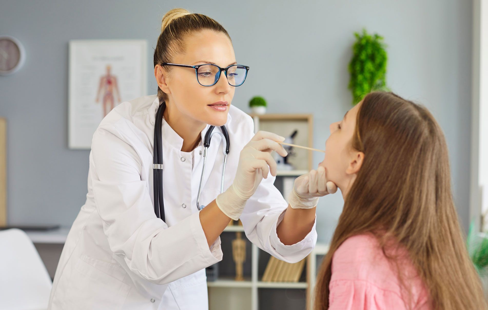 Doctor examining a child’s throat in a clinic with a tongue depressor