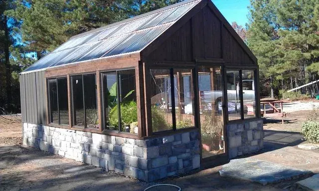 A greenhouse with a lot of windows and trees in the background.