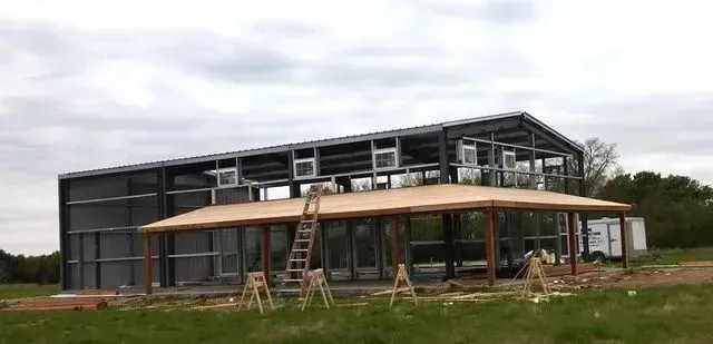 A large metal building with a porch is being built in a field.