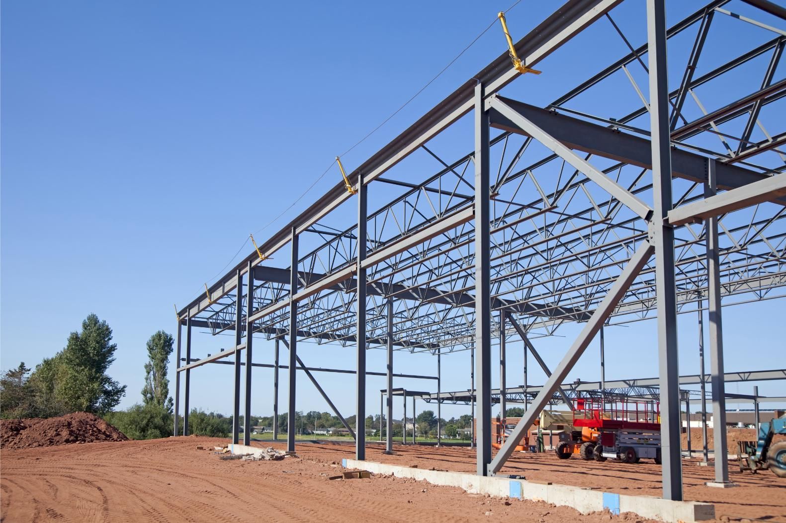 A large metal structure is being built on a dirt field.