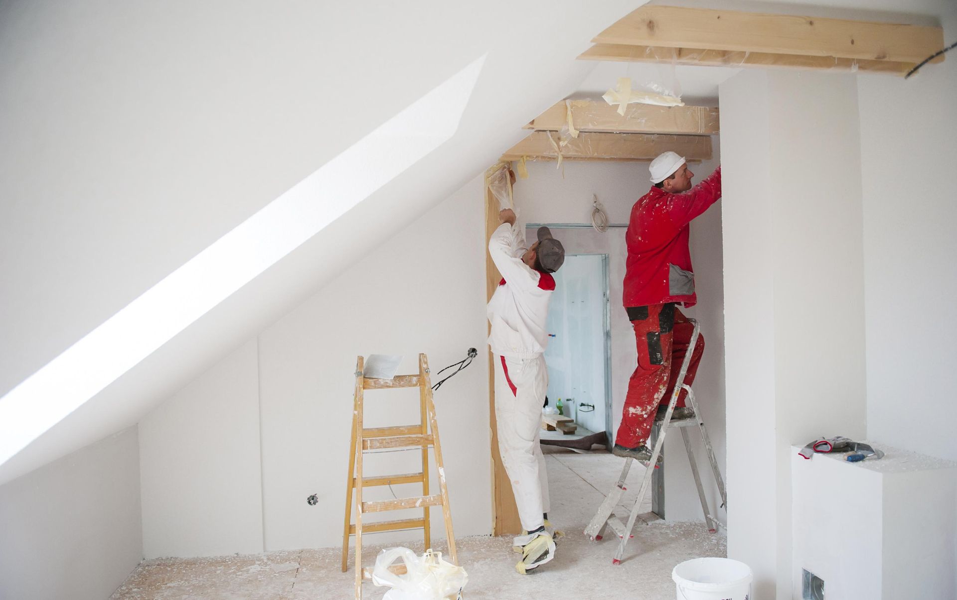 Two men are painting a wall in a room with a ladder.