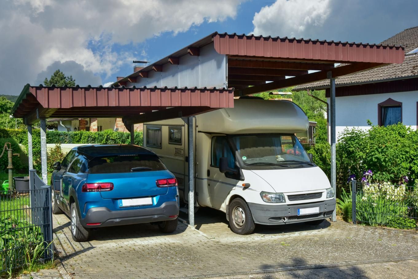 A blue car and a white van are parked under a carport.