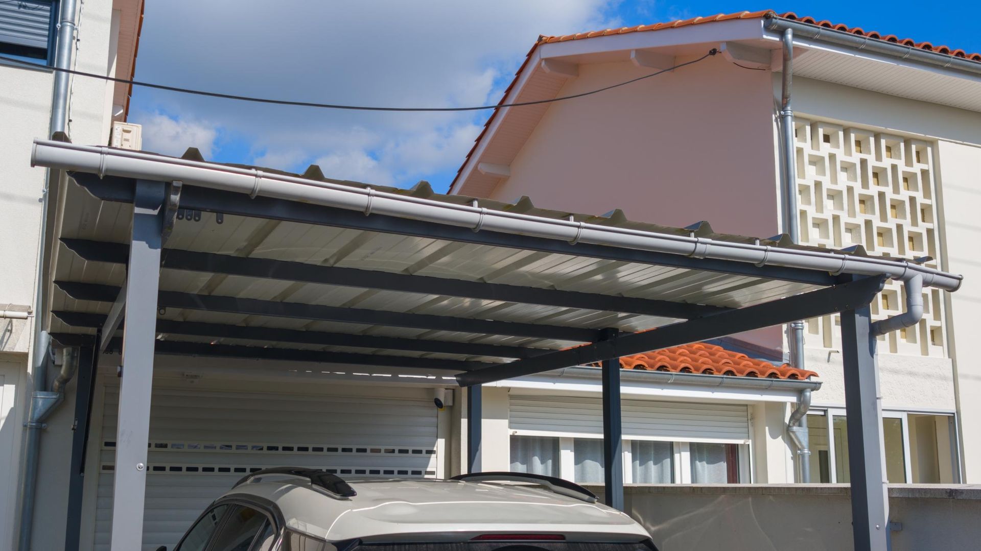 A car is parked under a canopy in front of a house.