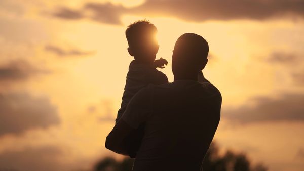 Silhouette of a person holding a child against a sunset background.
