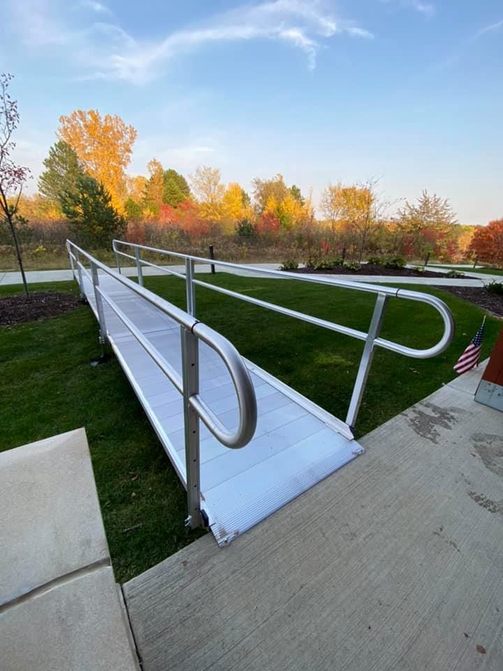 Outdoor wheelchair ramp with white railings and a concrete path in a park setting at sunset